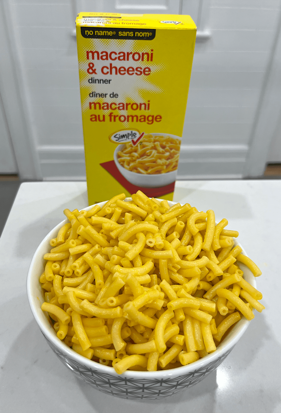 Bo\u00eete de macaronis au fromage de marque Sans Nom et un bol de macaronis pr\u00e9par\u00e9s.