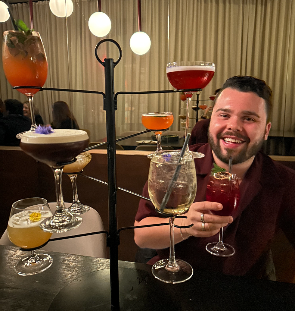 Brendan Mikan devant une structure m\u00e9tallique o\u00f9 7 cocktails sont suspendus.