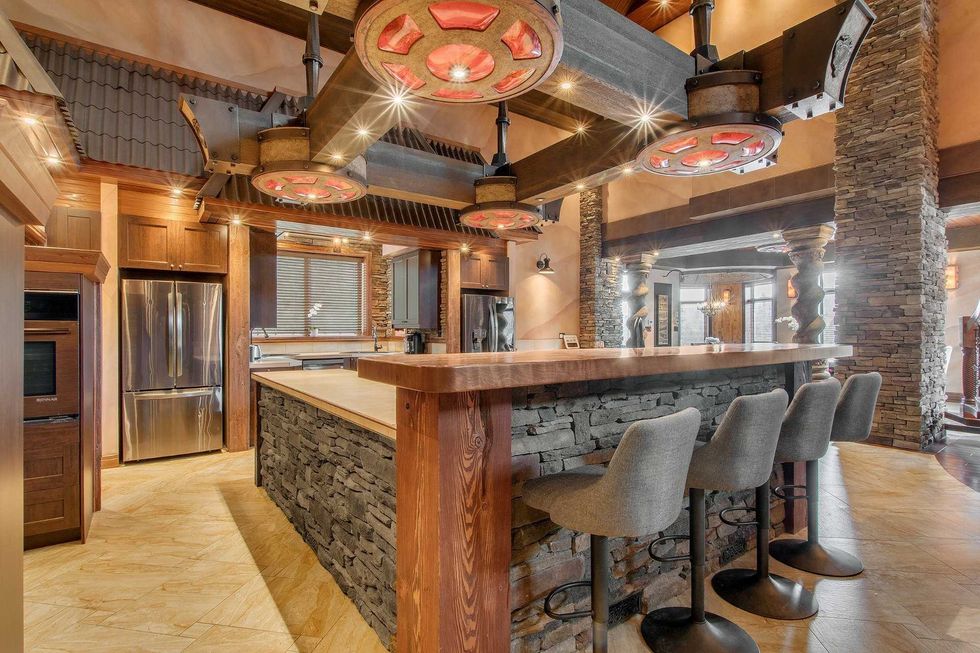 Cuisine avec grand \u00eelot en pierre et bois, hotte imposante et plafonds tr\u00e8s hauts.