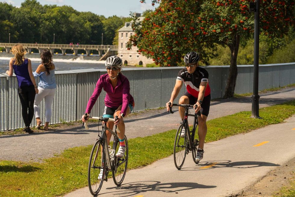 Cyclistes circulant sur une piste multifonctionnelle au bord de l\u2019eau par une journ\u00e9e ensoleill\u00e9e.