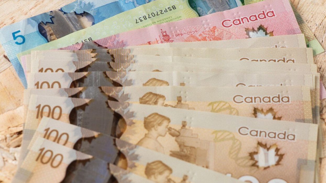 Des billets de 100 $ et d'autres billets d'argent canadien sont étalés sur une table en bois.