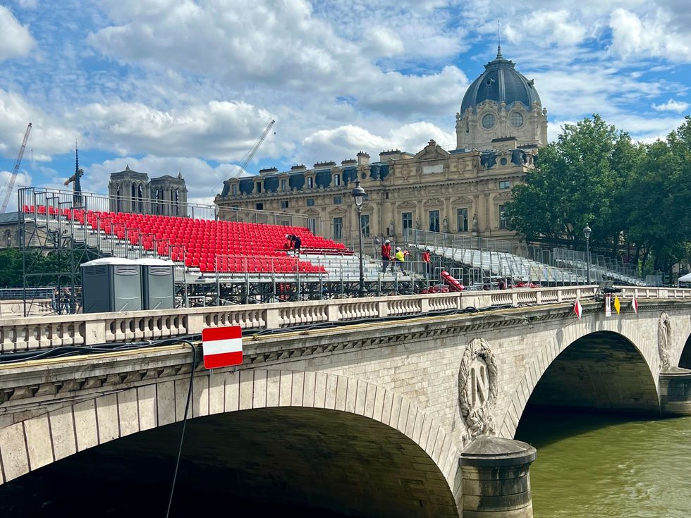 Des gradins avec des si\u00e8ges rouges sont install\u00e9s sur un pont surplombant un fleuve.