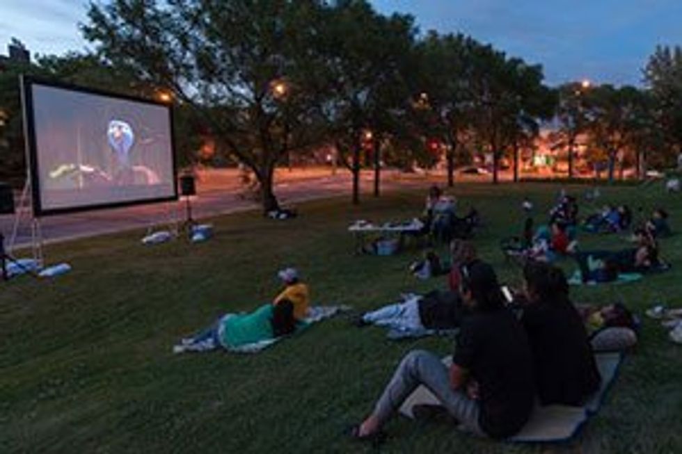 Des personnes assises dans le gazon qui regardent un film en plein air.