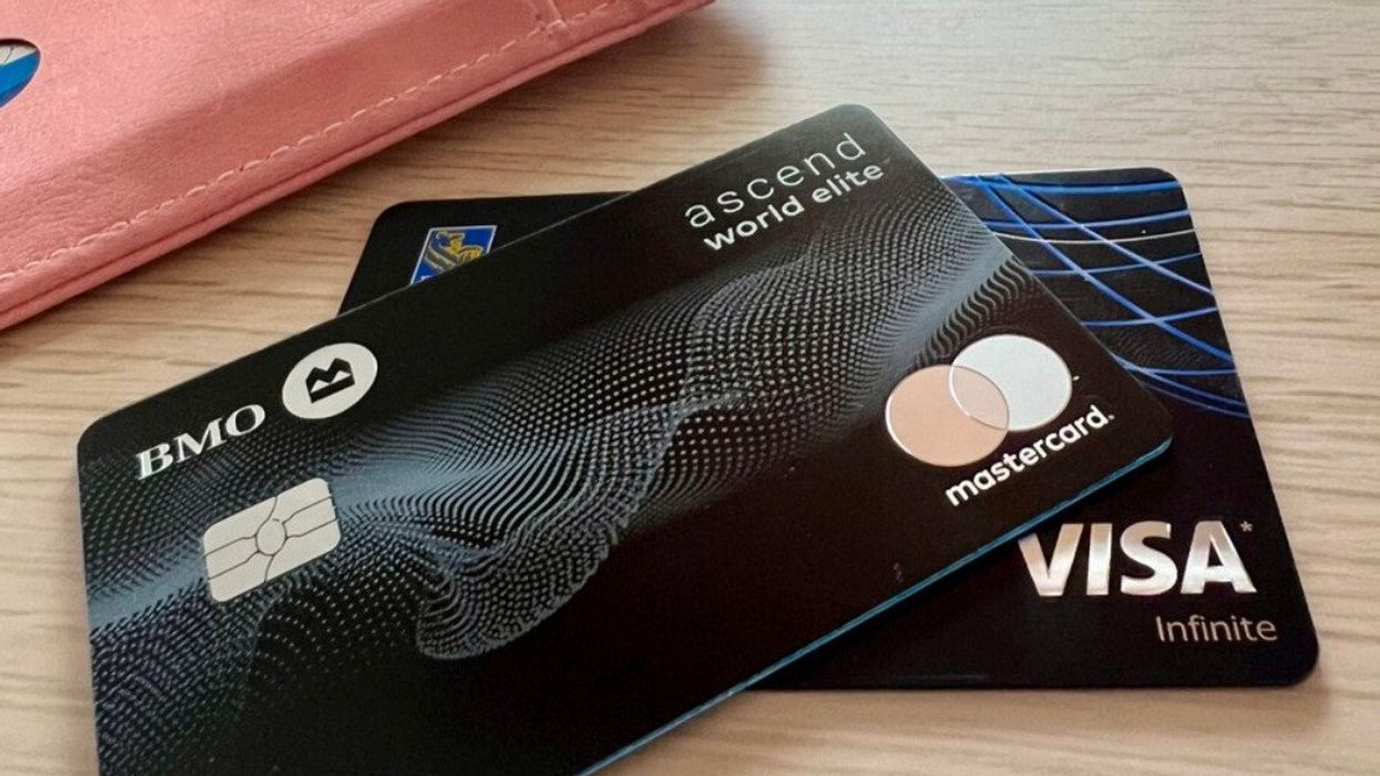 Deux cartes de crédit noires Visa et Mastercard sont placés sur une table en bois à côté d'un porte-cartes rose.