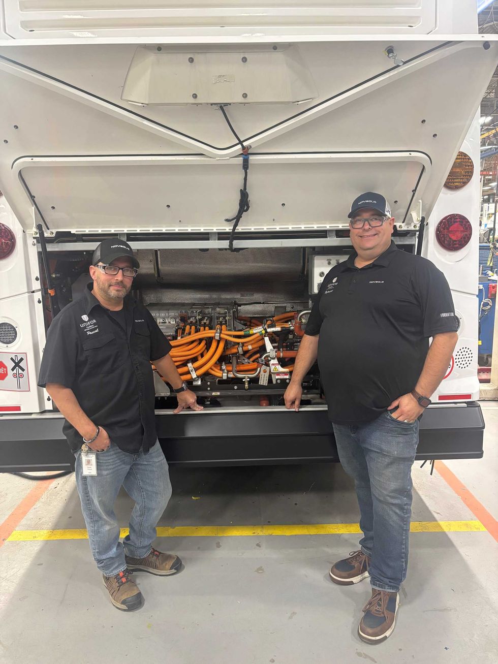 Deux employ\u00e9s de Nova Bus devant les composantes \u00e9lectriques d\u2019un autobus dans une usine.