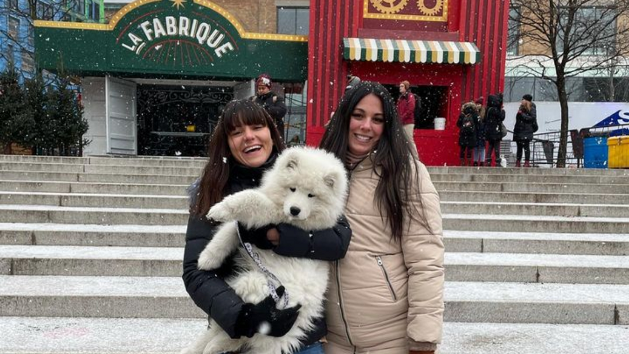 Deux personnes avec un chien blanc devant des décors verts et rouge du Grand Marché de Noël de Montréal.