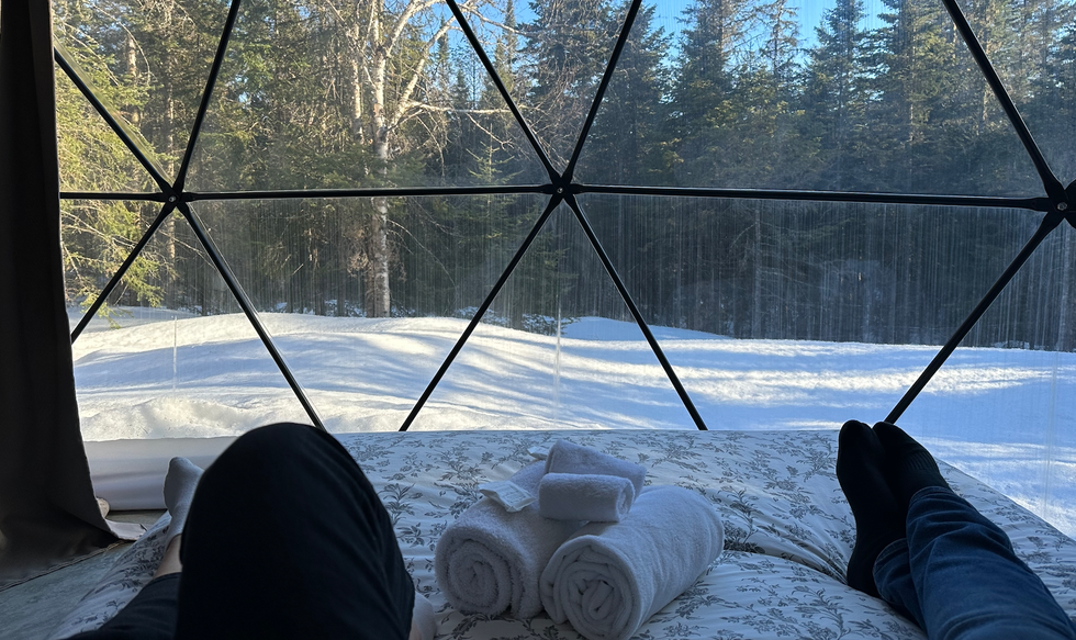 Deux personnes \u00e9tendues sur un lit avec des serviettes devant la toile transparente du d\u00f4me qui donne sur les arbres.