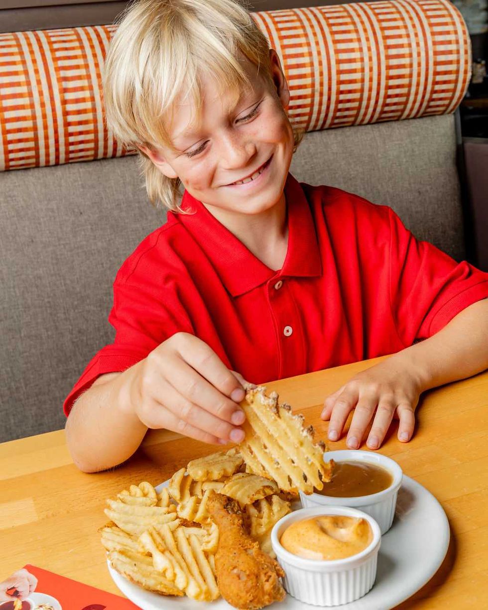 Enfant d\u00e9gustant des frites gaufr\u00e9es avec du poulet frit chez Scores.