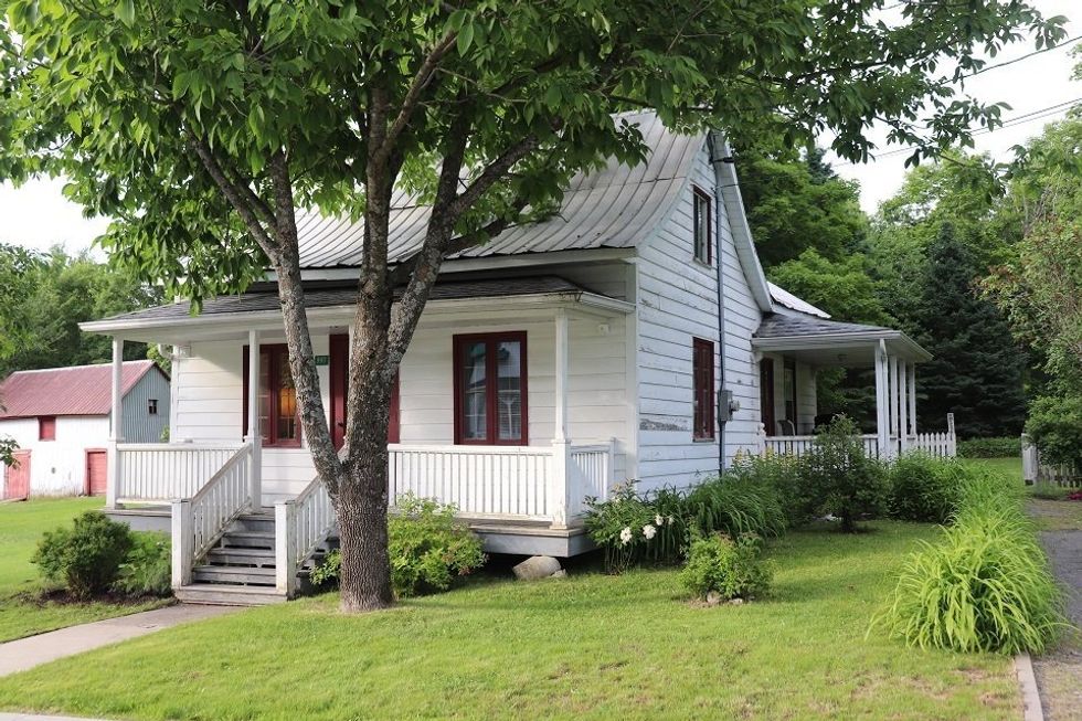 Fa\u00e7ade d'une maison \u00e0 \u00e9tages blanche avec une v\u00e9randa \u00e0 vendre au Qu\u00e9bec.