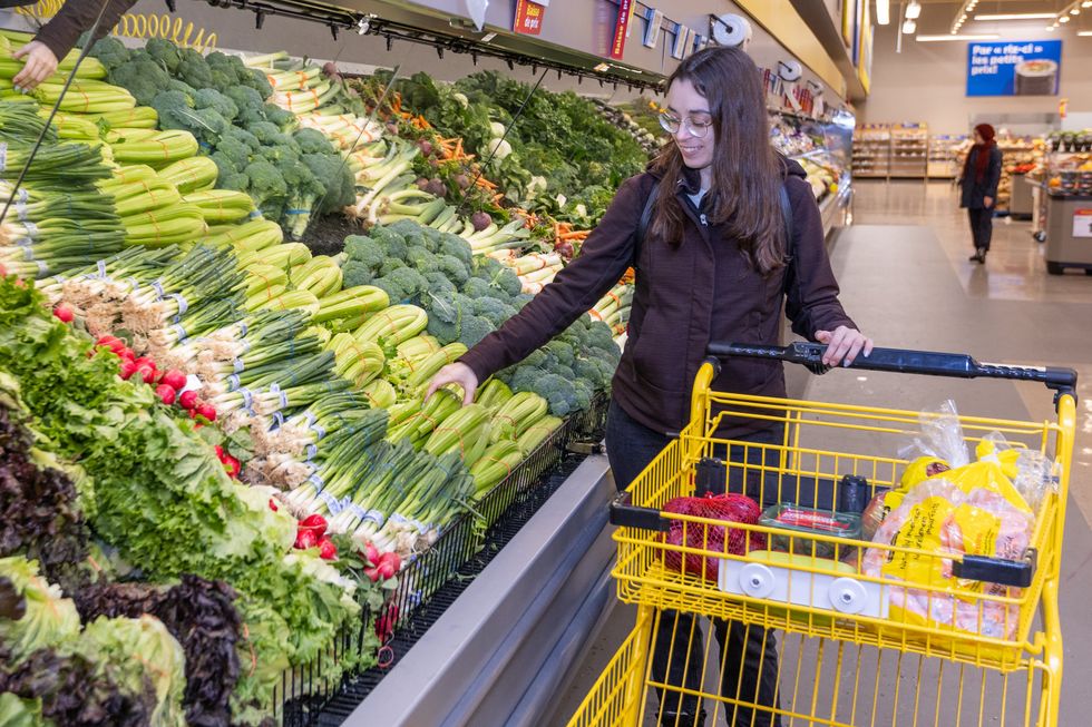 Femme faisant son \u00e9picerie chez Maxi, s\u00e9lectionnant des l\u00e9gumes frais dans l\u2019all\u00e9e des produits.