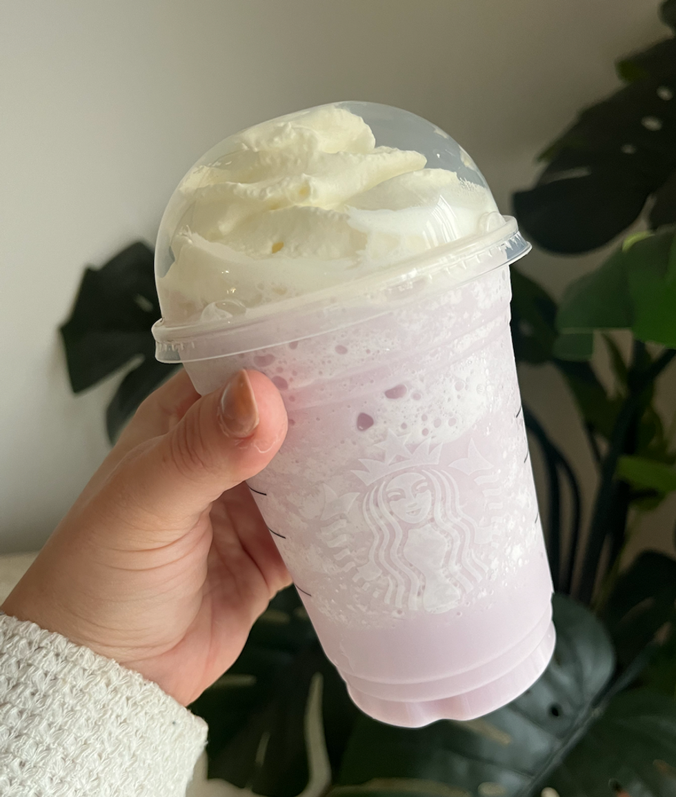 Frappuccino \u00e0 la lavande du Starbucks dans une main, garni de cr\u00e8me fouett\u00e9e.