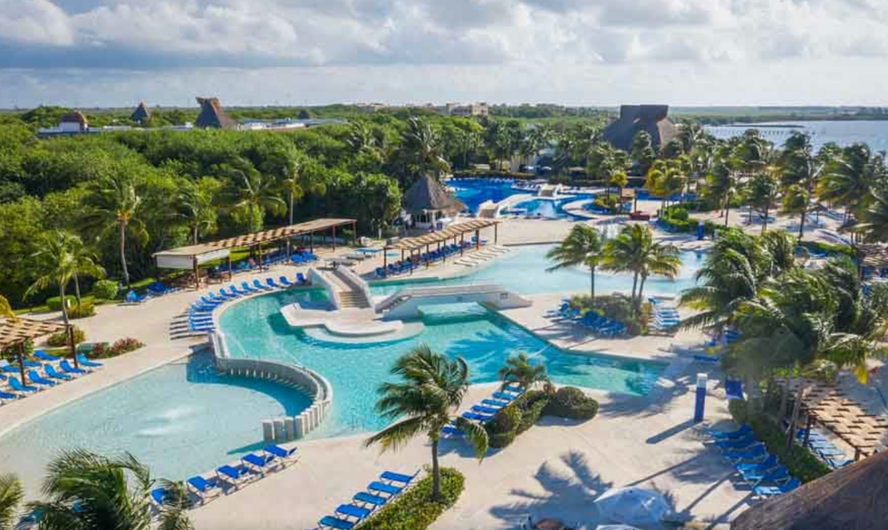Grande piscine entour\u00e9e de chaises longues et de palmiers.