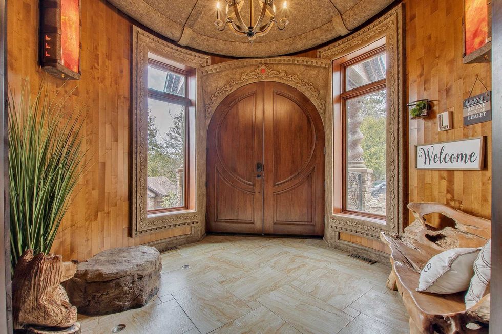 Hall d\u2019entr\u00e9e avec grande porte double arrondie en bois, moulures sculpt\u00e9es et fen\u00eatres lat\u00e9rales.