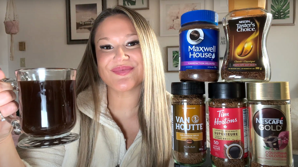 Izabelle Bee tient une tassé de café noir et pose à côté des cinq contenants de café instantané.
