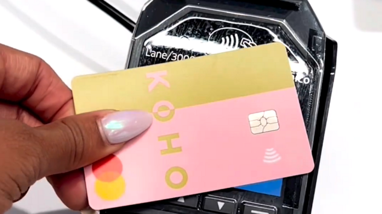 La main d'une personne utilisant la carte Koho Mastercard rose et dorée sur un terminal de paiement noir.