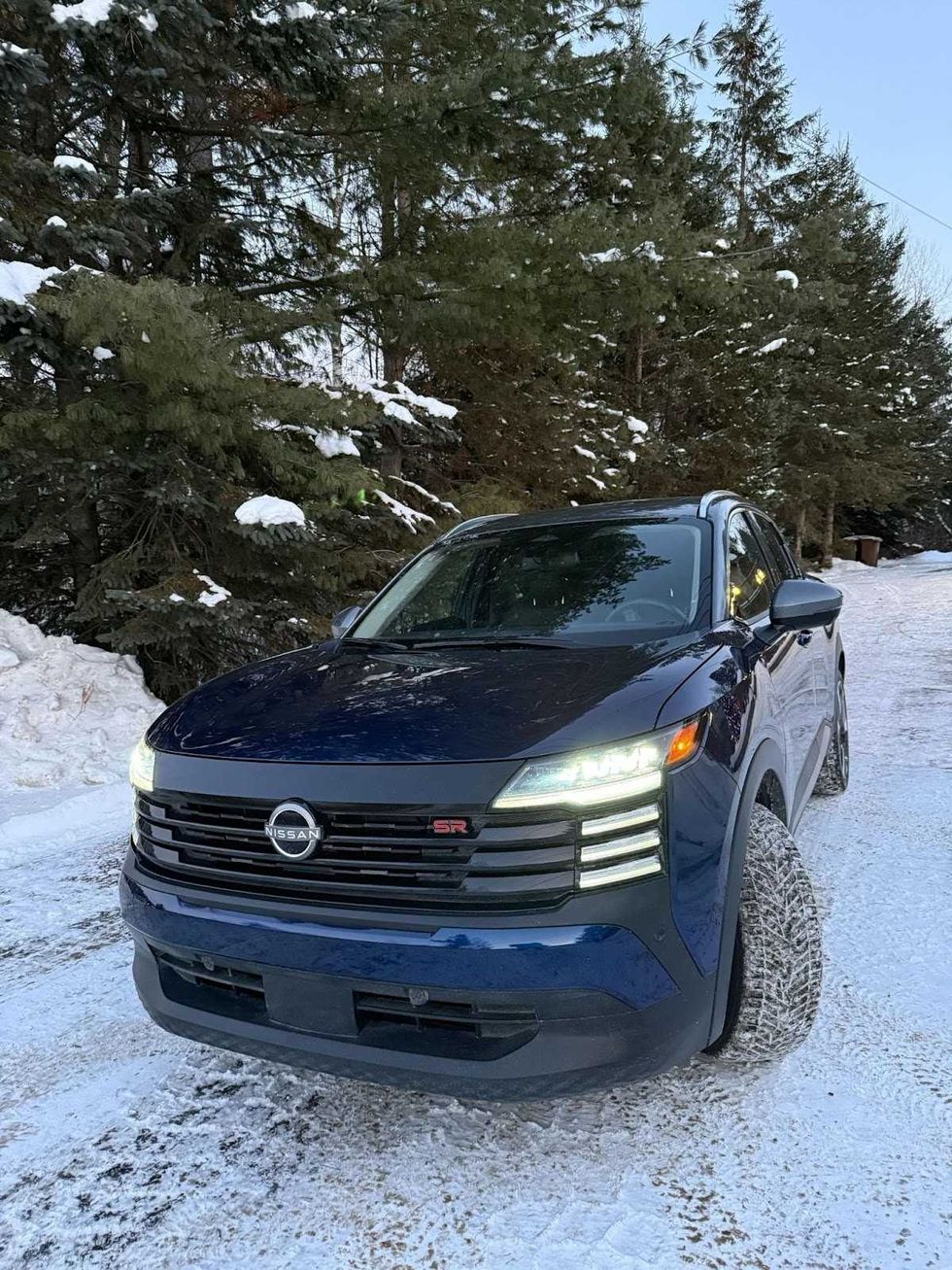 Le Nissan KICKS sur une route enneig\u00e9e, devant des arbres.