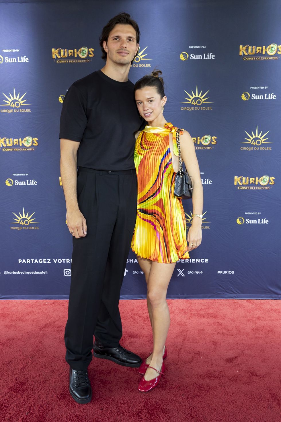 Lucie Rh\u00e9aume Gonzalez, v\u00eatue d'une robe jaune, et son amoureux tout en noir sur le tapis rouge de Kurios du Cirque du Soleil.