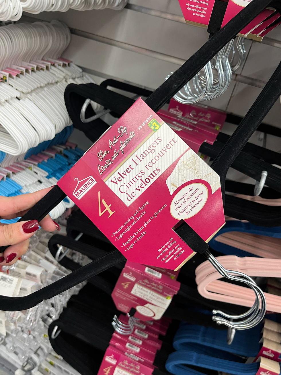 Main qui tient des cintres recouverts de velours noir en paquet de quatre.