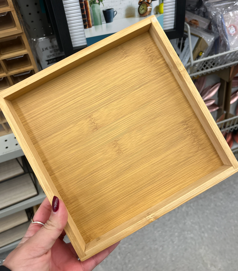 Main qui tient un plateau d\u00e9coratif carr\u00e9 en bois.