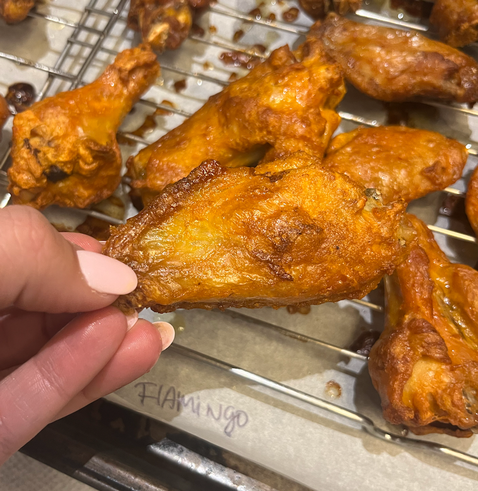 Main qui tient une aile de poulet de la marque Flamingo.