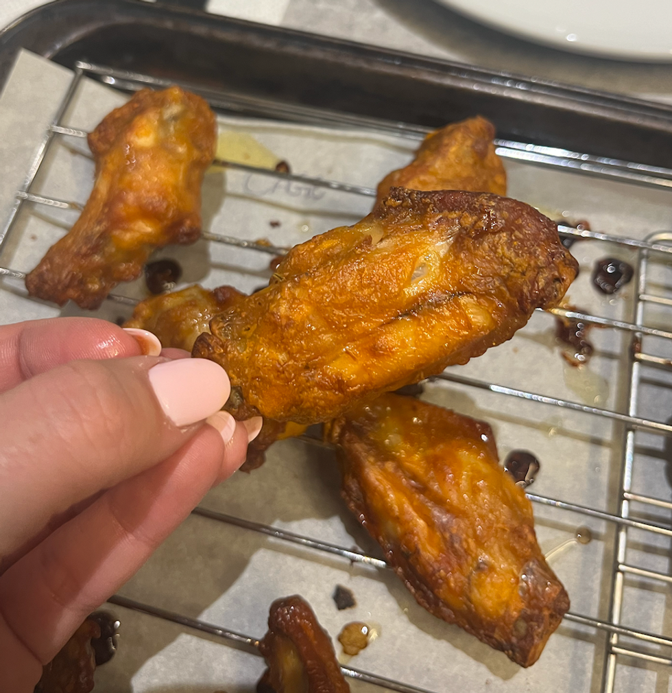 Main qui tient une aile de poulet de la marque La Cage.