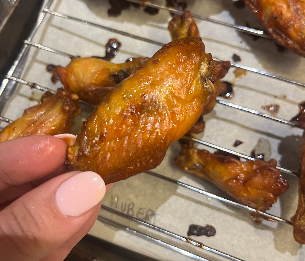 Main qui tient une aile de poulet de St-Hubert.