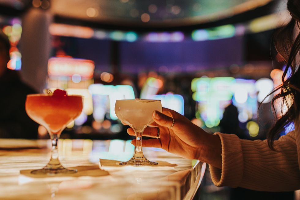 Main tenant un cocktail servi au bar, avec des machines de loterie en arri\u00e8re-plan.