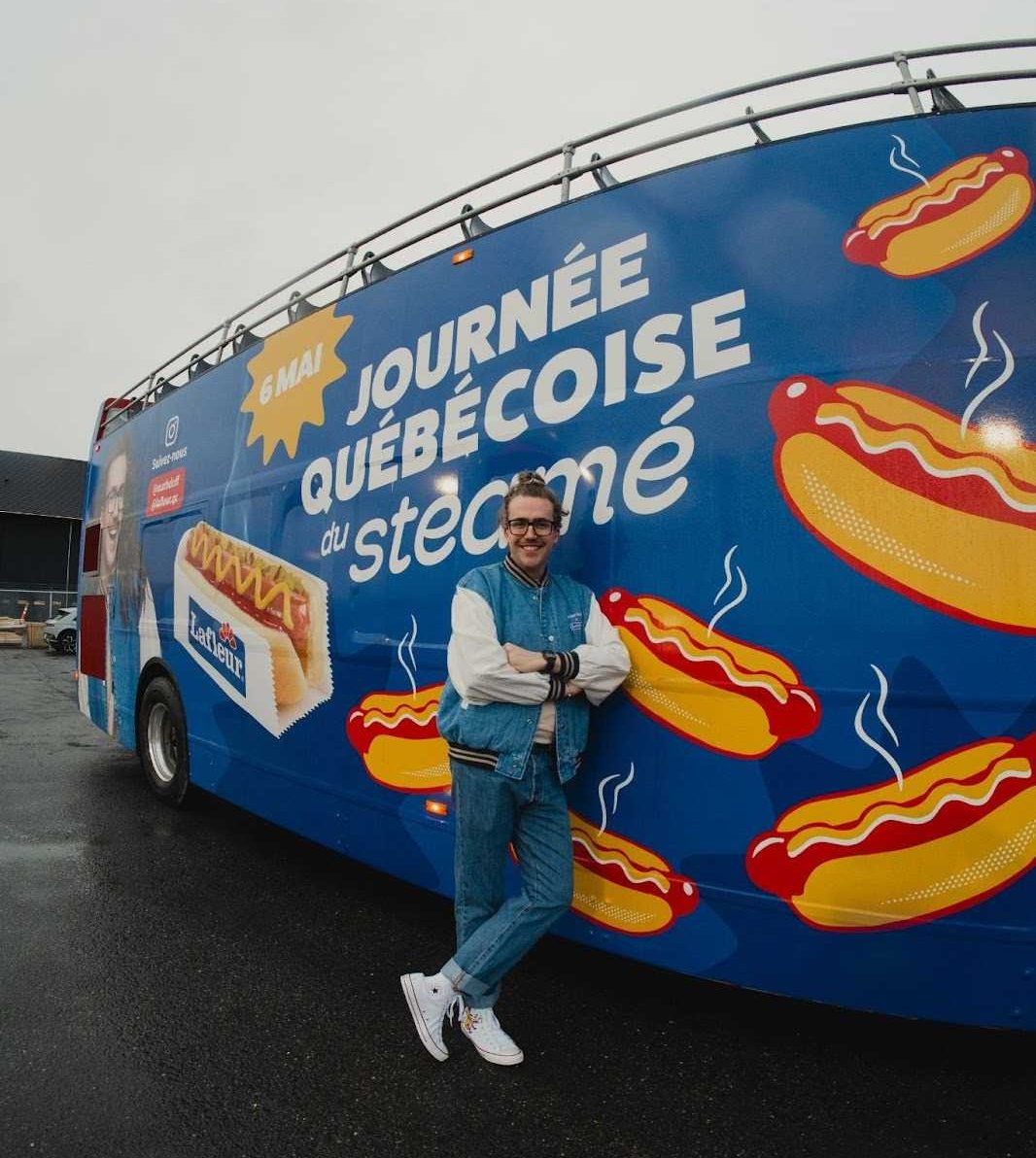 Mathieu Dufour est appuy\u00e9 contre un autobus d\u00e9cor\u00e9 de hot-dogs sur lequel on peut lire \u00ab Journ\u00e9e qu\u00e9b\u00e9coise du steam\u00e9 \u00bb.