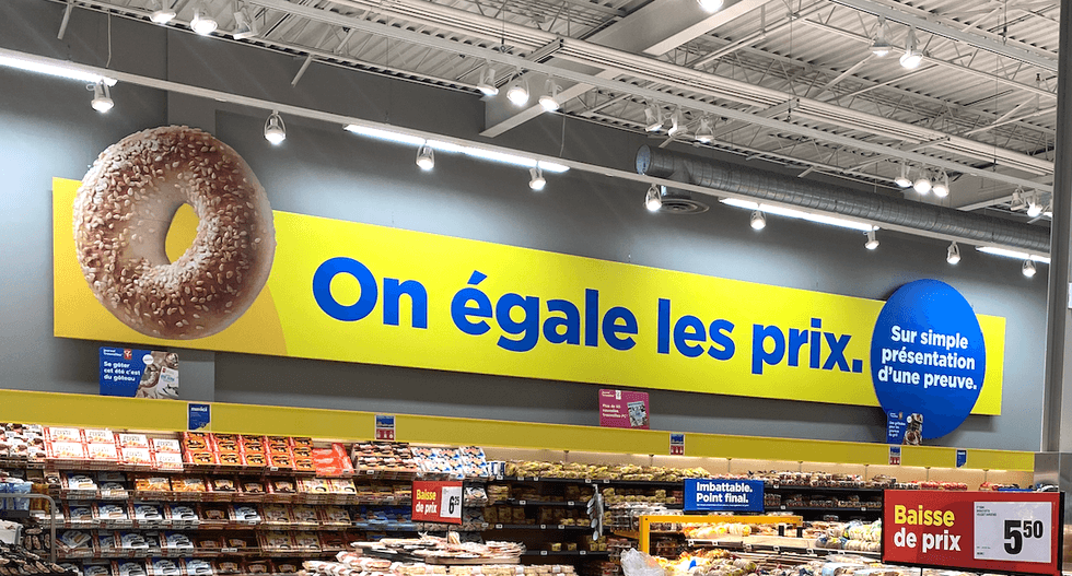 Pancarte jaune et bleue dans un Maxi indiquant \u00ab On \u00e9gale les prix. Sur simple pr\u00e9sentation d'une preuve. \u00bb avec l'image d'un bagel.