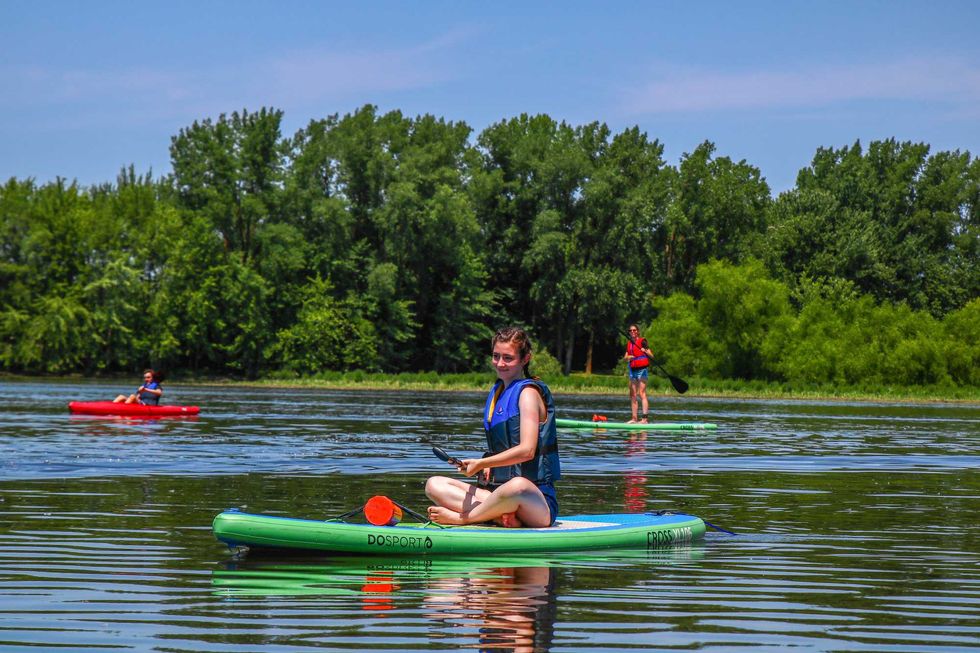 Personnes pratiquant la planche \u00e0 pagaie et le kayak sur une rivi\u00e8re bord\u00e9e d\u2019arbres.