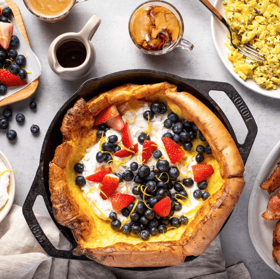 Petit-d\u00e9jeuner sucr\u00e9 compos\u00e9 de bleuets et de fraises, accompagn\u00e9 de caf\u00e9, d'\u0153ufs et de bacon dispos\u00e9s sur la table.