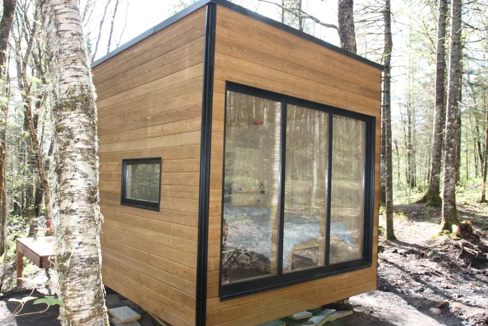 petit g\u00eete en cube au milieu des arbres avec une grande fen\u00eatre.