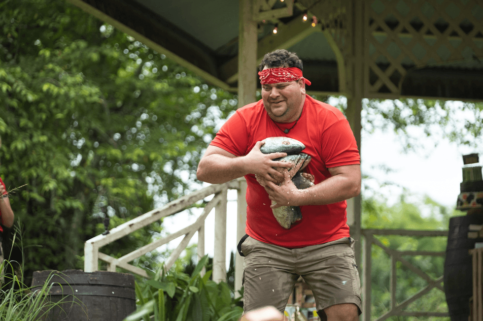 Philippe Laprise en pleine course avec un chargement de poissons dans les bras lors d'un d\u00e9fi dans Sortez-moi d'ici!
