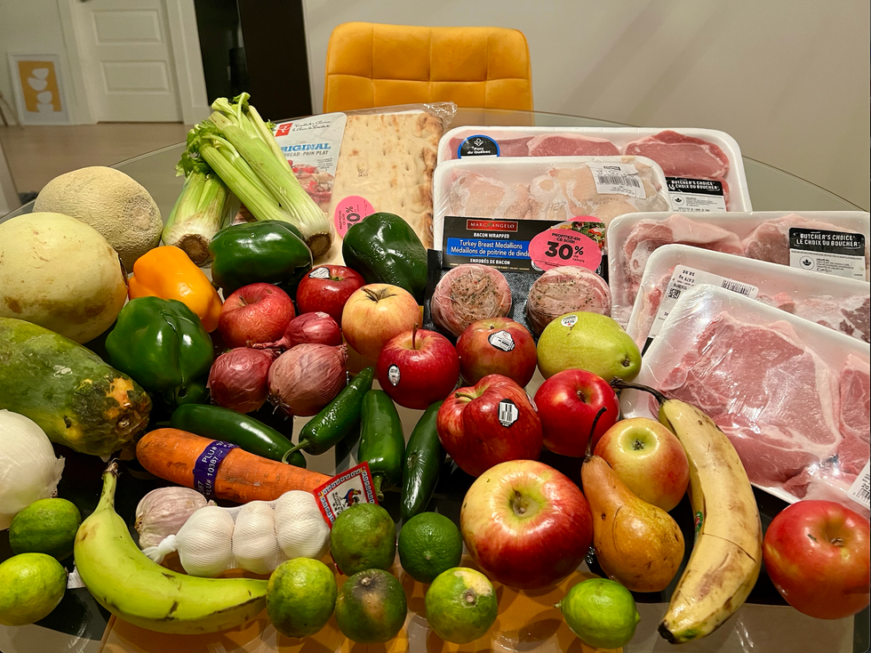 Photo de plusieurs produits d'\u00e9picerie (viande, pain, fruits et l\u00e9gumes) \u00e9tal\u00e9s sur une table.