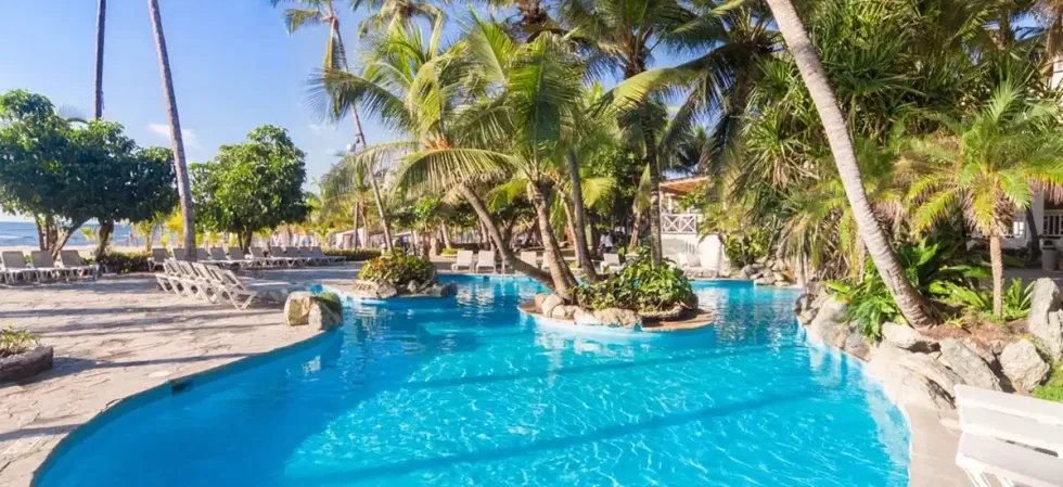 Piscine aux eaux turquoise bord\u00e9e de palmiers et de chaises longues, avec acc\u00e8s direct \u00e0 la plage au Coral Costa Caribe.