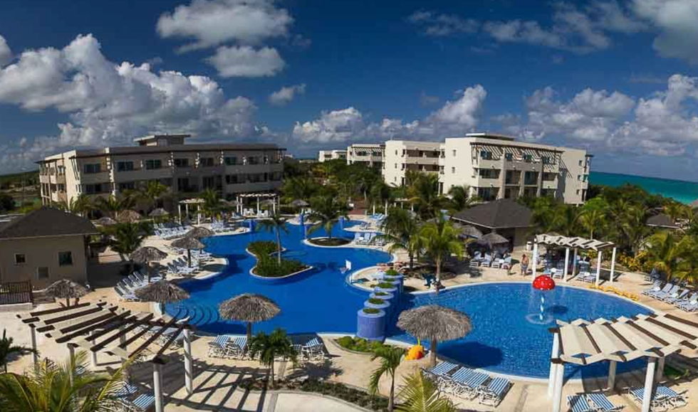 Piscine avec palmiers, chaises longues et vue sur la mer.
