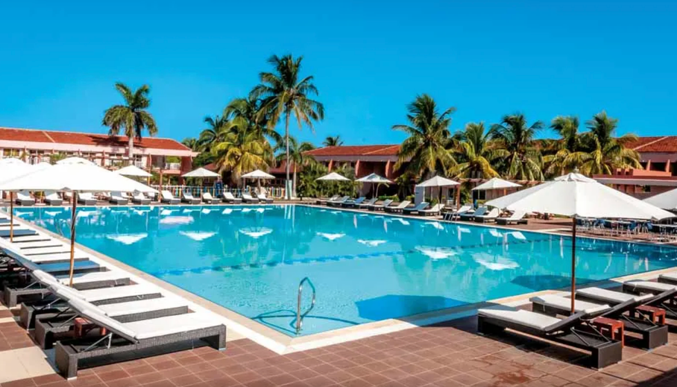 Piscine centrale avec palmiers et chaises longues.