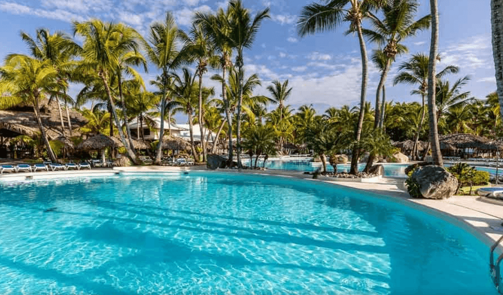 Piscine d'un h\u00f4tel entour\u00e9e de chaises longues et de palmiers.