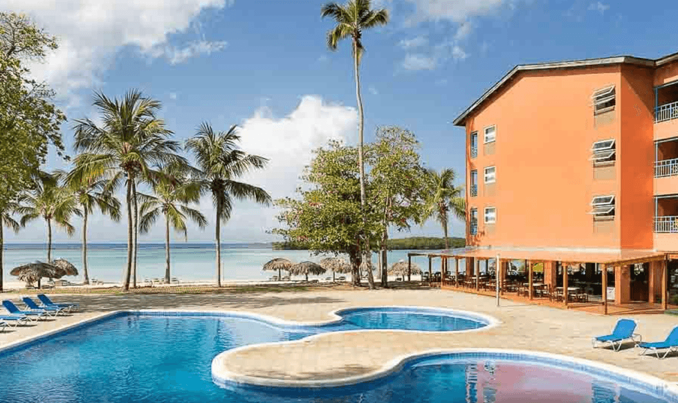 Piscine d'un h\u00f4tel entour\u00e9e de chaises longues et de palmiers.