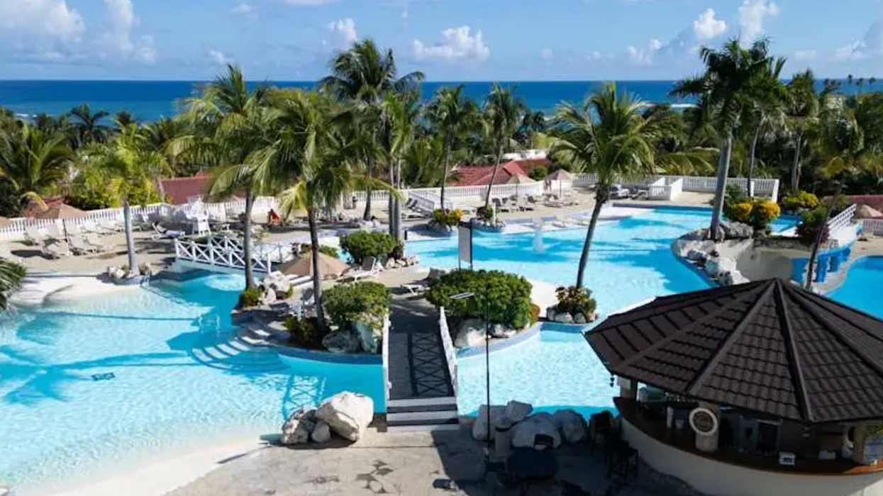 Piscines en forme de lagon entourées de palmiers, de ponts et d’espaces détente, avec vue sur l’océan au Cofresi Palm Beach Resort and Spa.