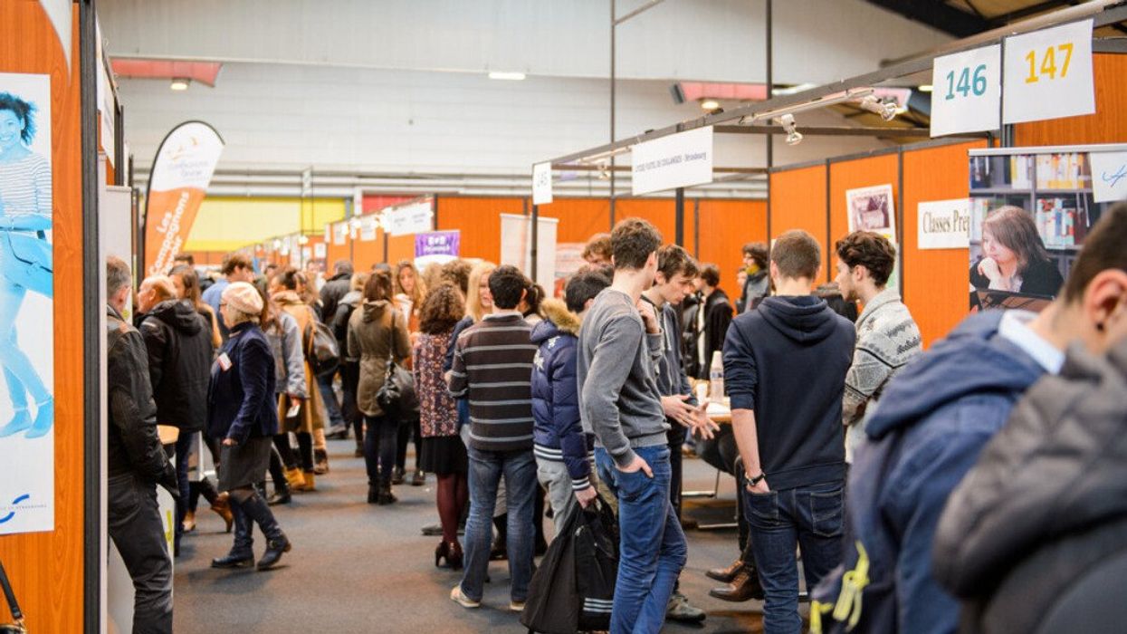 Plusieurs personnes sont debout entre les kiosques d'une foire de l'emploi.