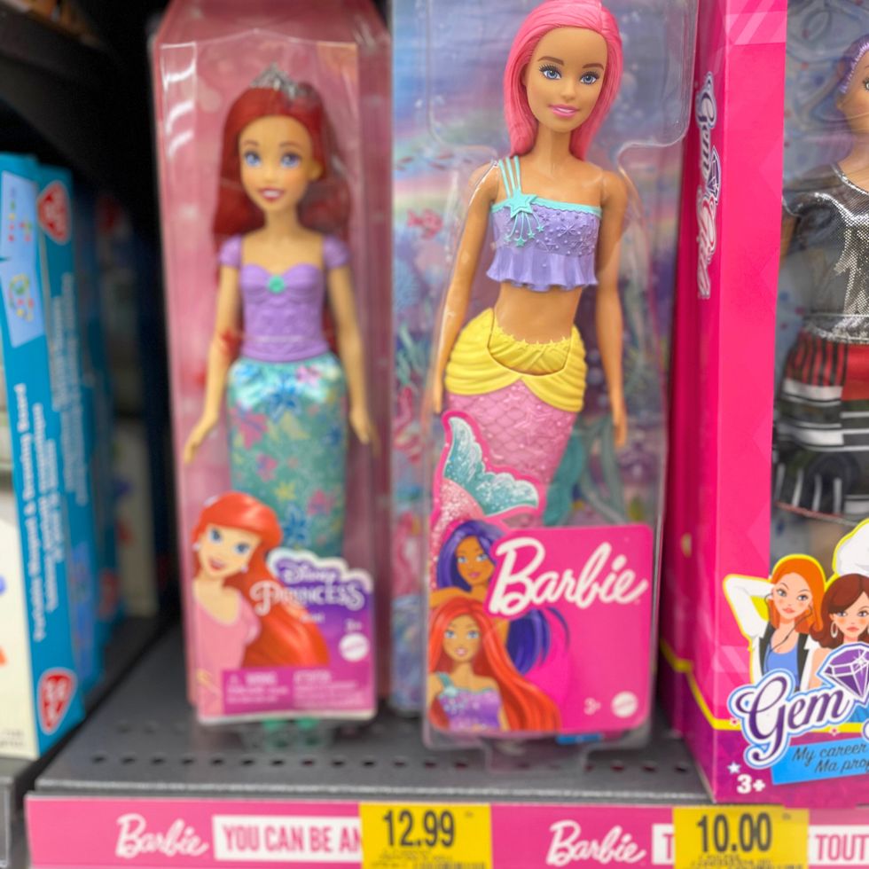 Plusieurs poup\u00e9es Barbie sur une \u00e9tag\u00e8re de magasin.