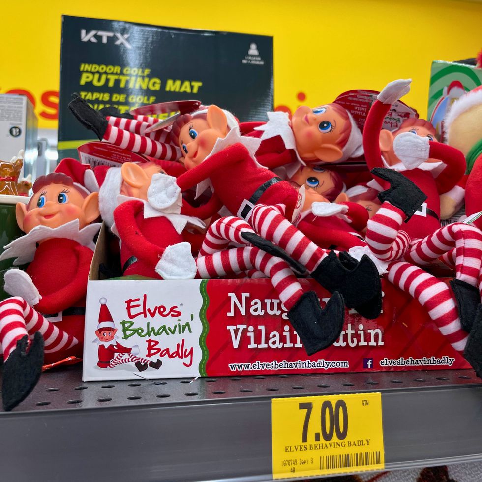 Plusieurs poup\u00e9es lutins festives sont empil\u00e9es sur une \u00e9tag\u00e8re de magasin.