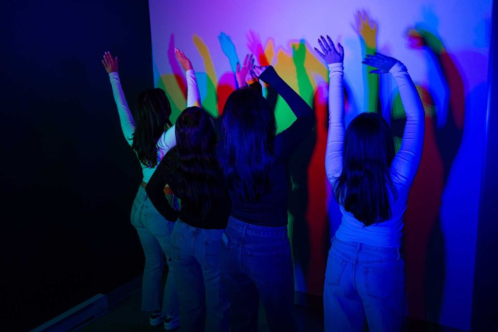 Quatre femmes cr\u00e9ant des ombres color\u00e9es dans la salle RGB du Mus\u00e9e de l\u2019Illusion Montr\u00e9al, une installation immersive et interactive \u00e0 Montr\u00e9al.