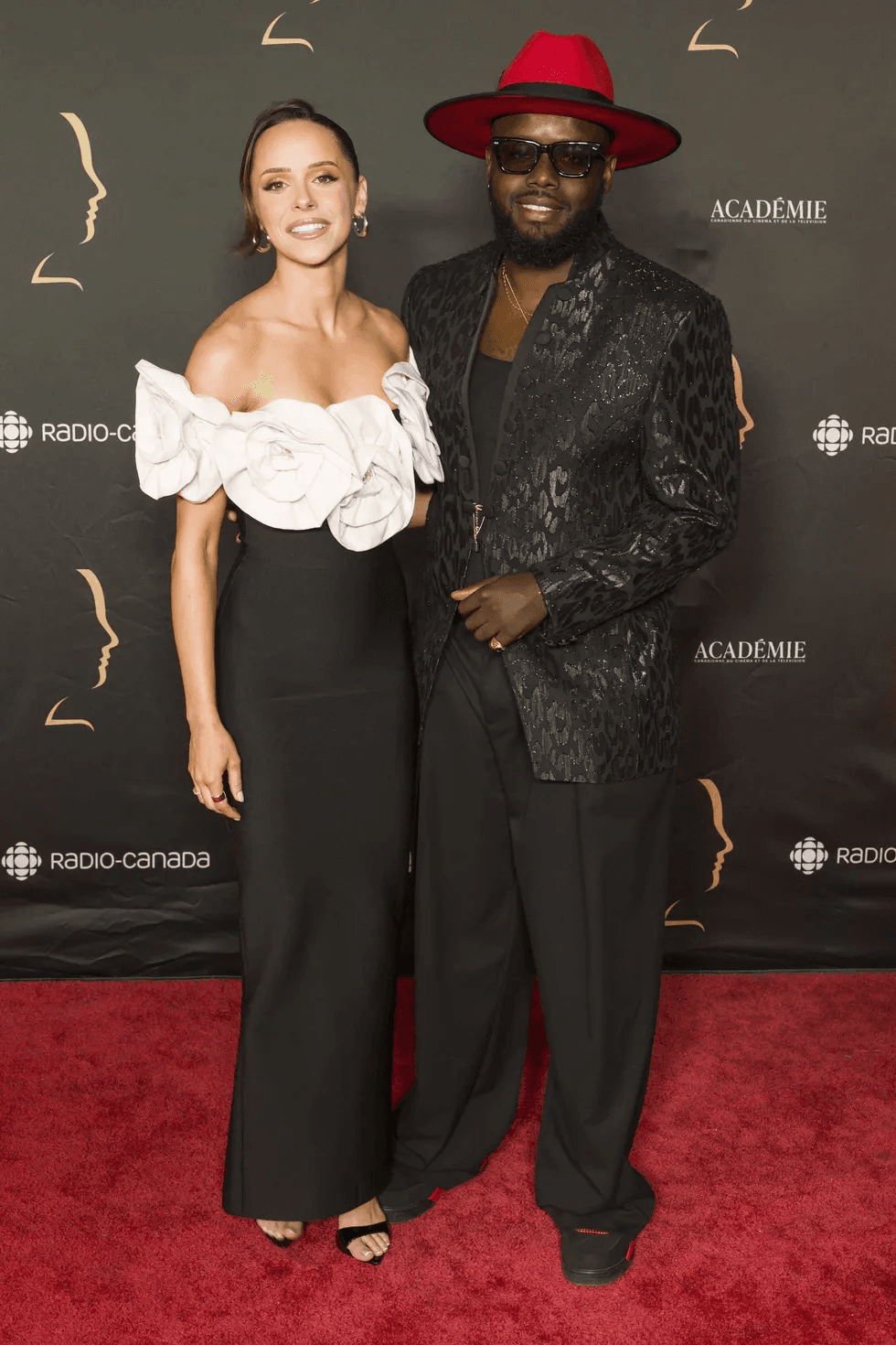 Sabrina Adams, en robe noire \u00e0 volant floral blanc, pose aux c\u00f4t\u00e9s d'Olivier Louissaint, en veston et chapeau rouge, sur le tapis rouge des prix G\u00e9meaux.