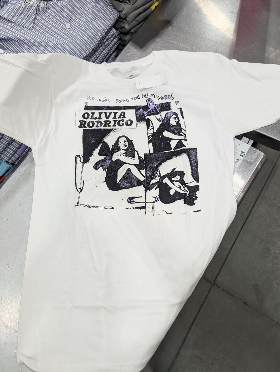 T-shirt blanc avec imprim\u00e9 noir et violet d'Olivia Rodrigo vendu dans le rayon mode chez Costco.