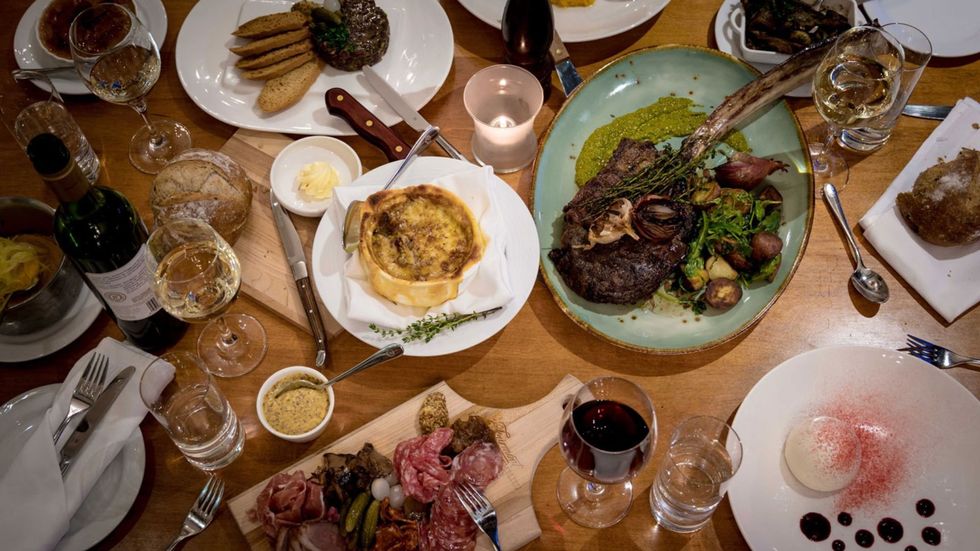 Table garnie d'une vari\u00e9t\u00e9 de mets, incluant des assiettes de viande et de charcuterie, des tartelettes, des tartares, des desserts et des vins.