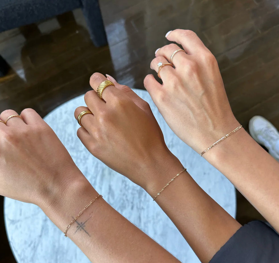 Trois poignets, chacun orn\u00e9s d'un mince bracelet en cha\u00eene dor\u00e9e.