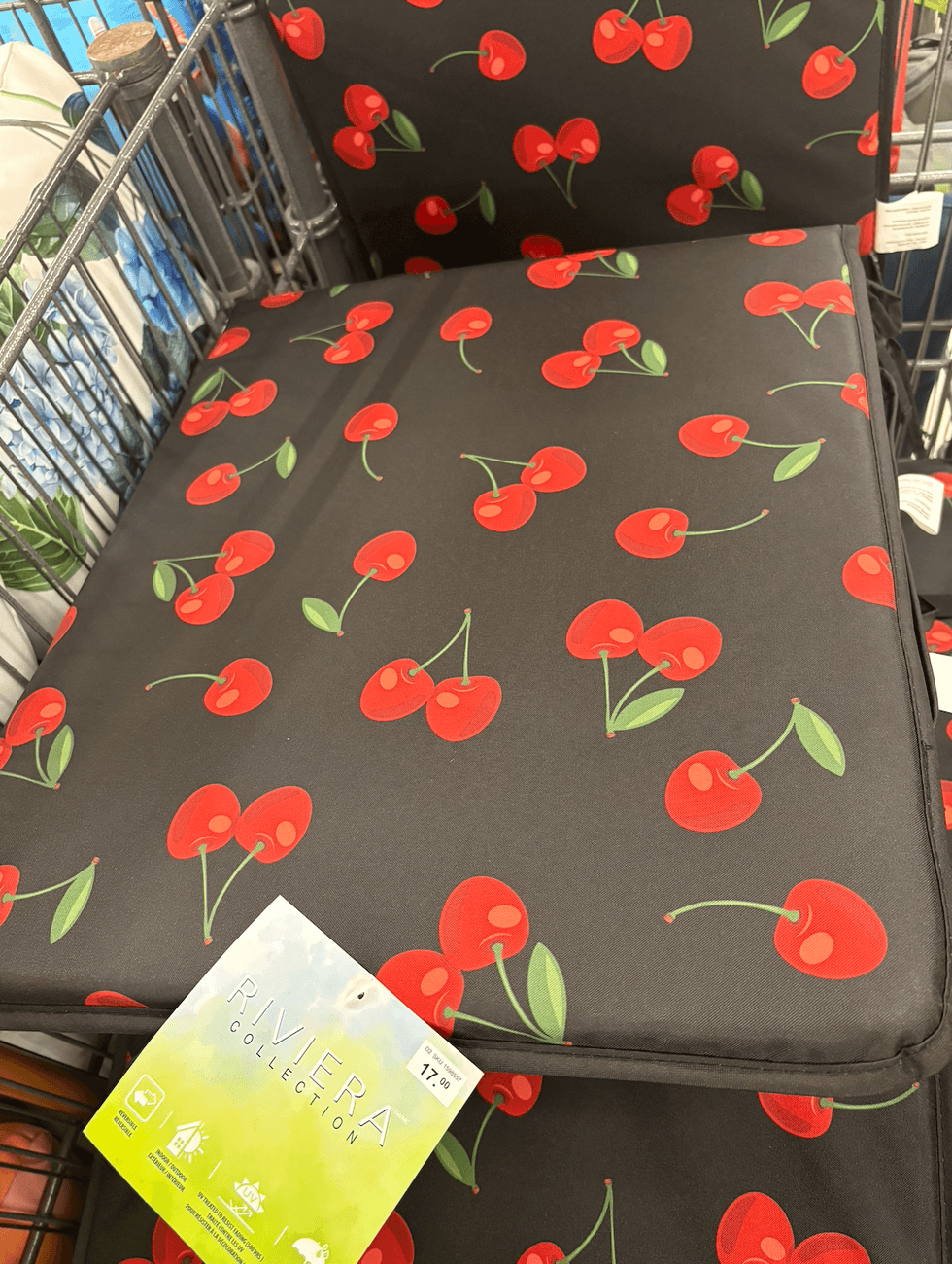 Un coussin noir pour chaise ext\u00e9rieure recouvert d'un imprim\u00e9 de petites cerises rouges.