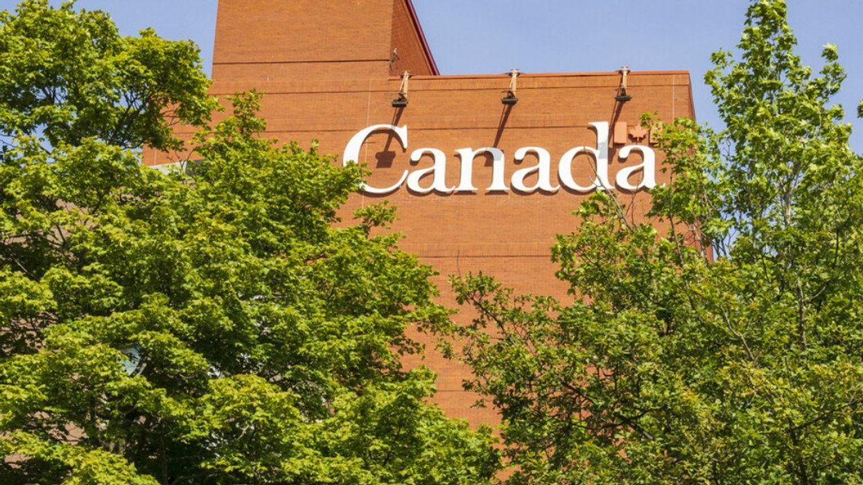 Un édifice avec le logo du gouvernement du Canada derrière des arbres.